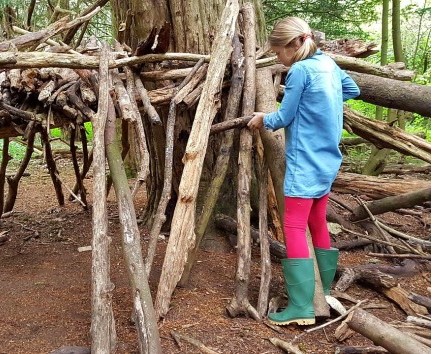 A girl adjusts a branch as she builds her own den around the trunk of a tree