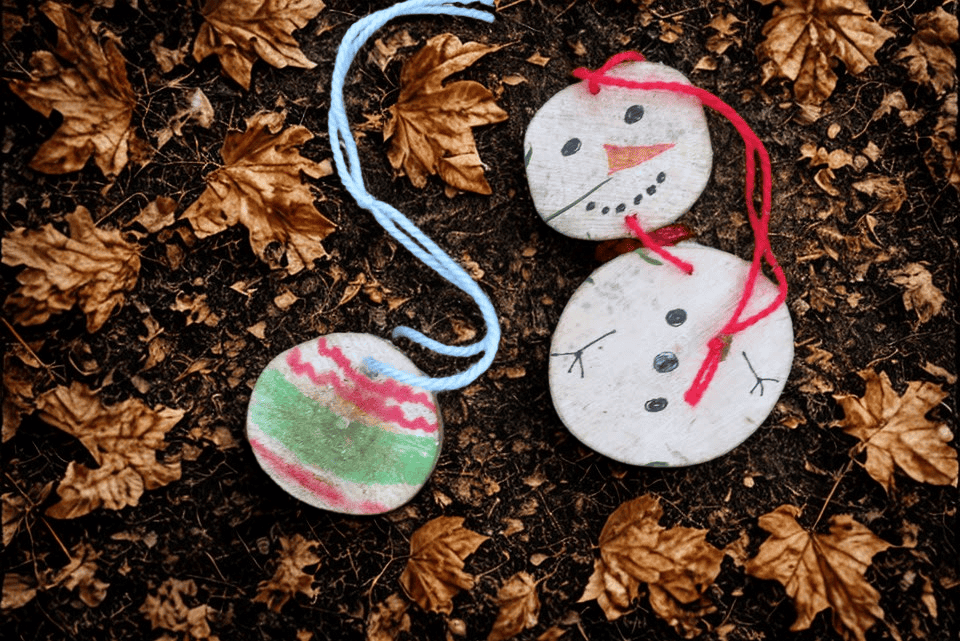 two fun handmade wooden decorations, a bauble and a snowman, sit on the forest floor