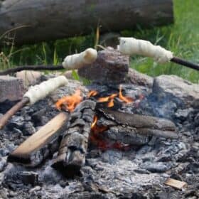 three sticks of damper bread are cooking on an open fire